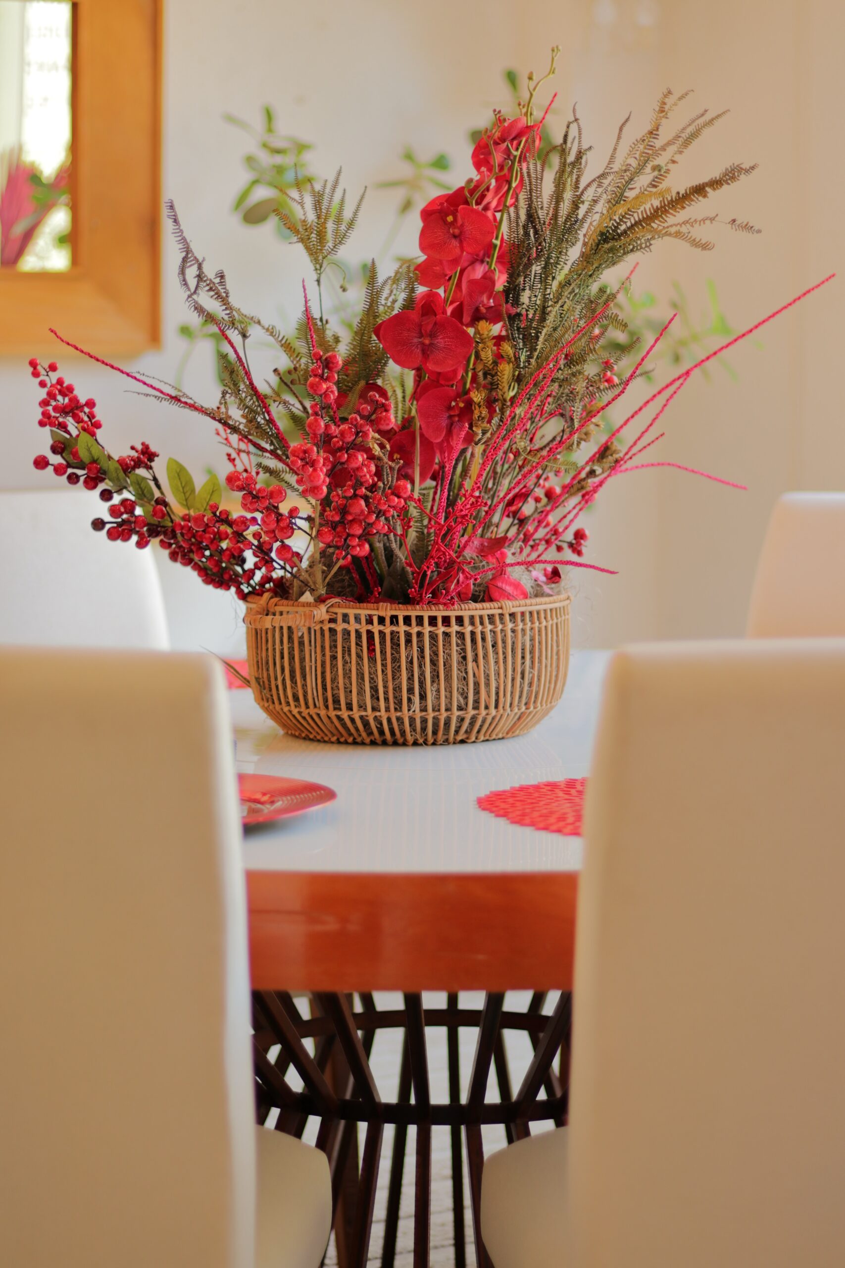 mesa branca com cadeiras brancas e arranjo floral vermelho e verde sobre a mesa